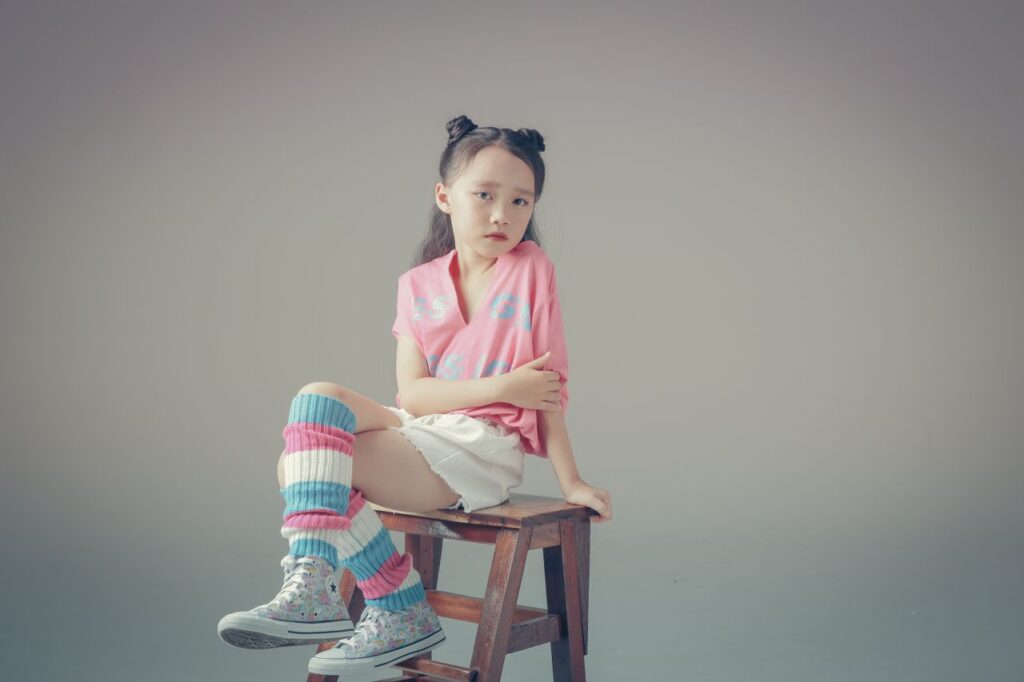 The Art of Drawing Readers In: Your attractive post title goes here Chic studio photograph of a young girl in colorful fashion sitting on a wooden stool against a neutral background.