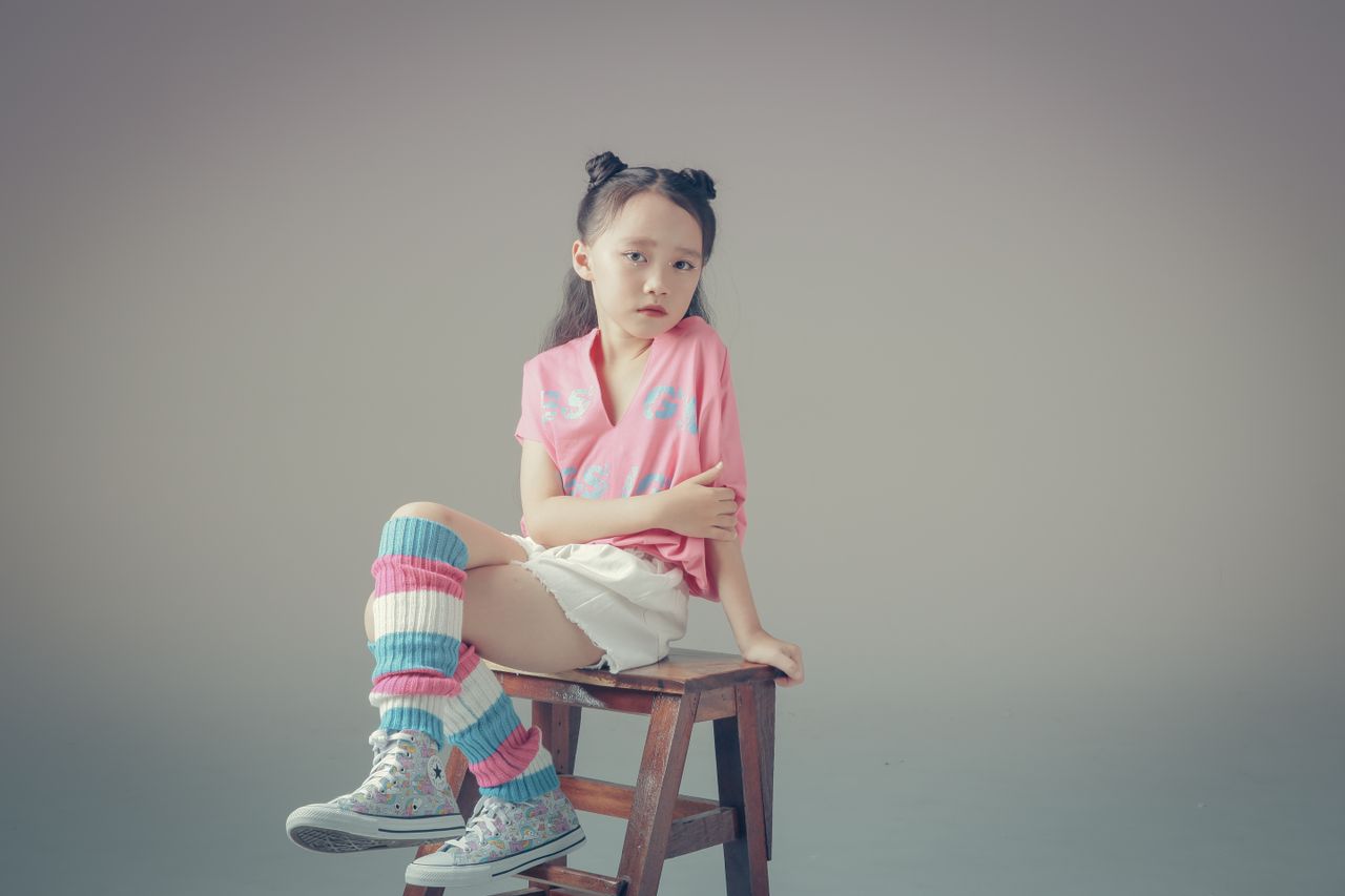 The Art of Drawing Readers In: Your attractive post title goes here Chic studio photograph of a young girl in colorful fashion sitting on a wooden stool against a neutral background.