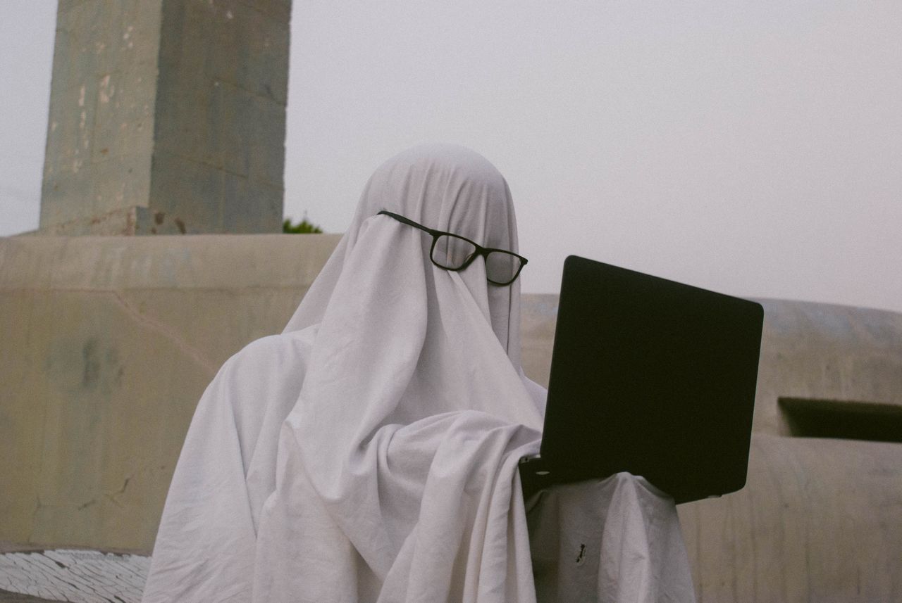 Crafting Captivating Headlines: Your awesome post title goes here A humorous depiction of a person in a ghost costume using a laptop outdoors.